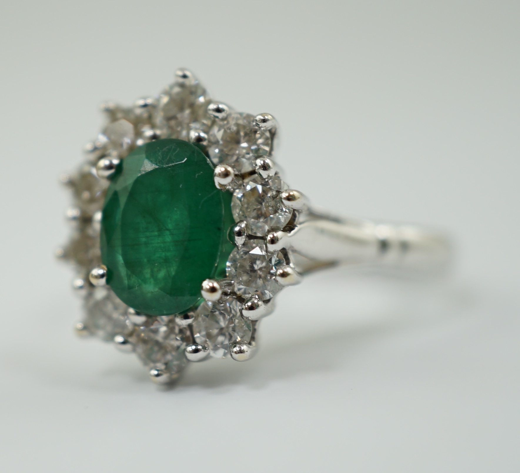 A modern 18ct white gold, single stone oval cut emerald and ten stone diamond set oval cluster ring